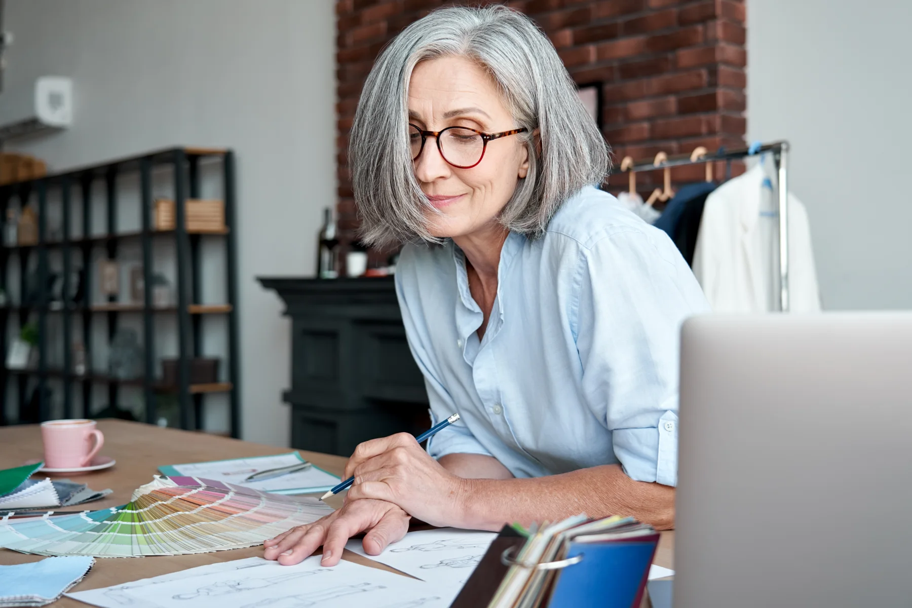 A mature woman reviewing fabric samples and sketches at her studio desk